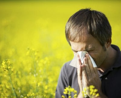 Man blowing nose in a field of flowers because of allergies