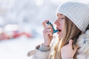 Woman using an inhaler outside in the cold for asthma
