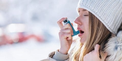 Woman using an inhaler outside in the cold for asthma