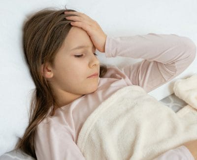 child laying in bed sick holding head because of sinus infection