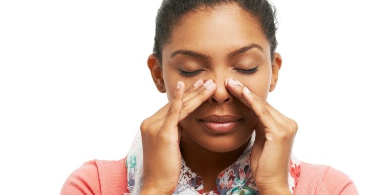 Young woman pressing on cheeks battling sinus problems while isolated on a white background