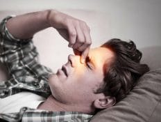 Man laying down holding bridge of nose with facial pain and headache