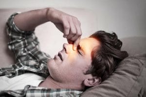 Man laying down holding bridge of nose with facial pain and headache