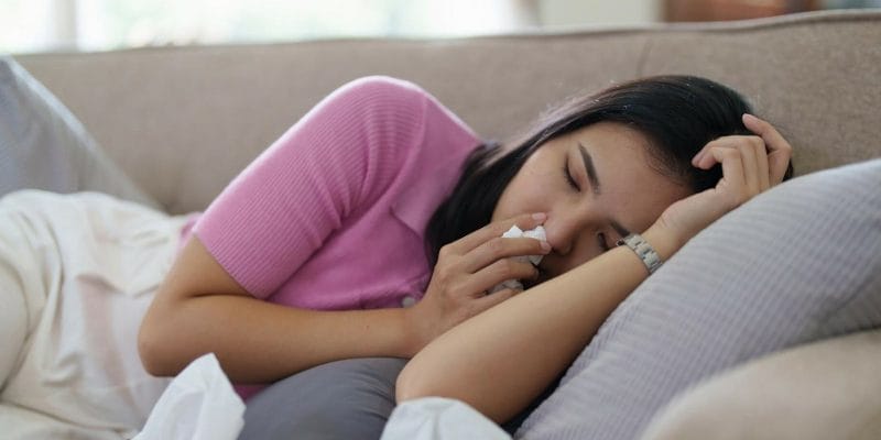 Woman laying on cough holding tissue to nose with dizziness and headache